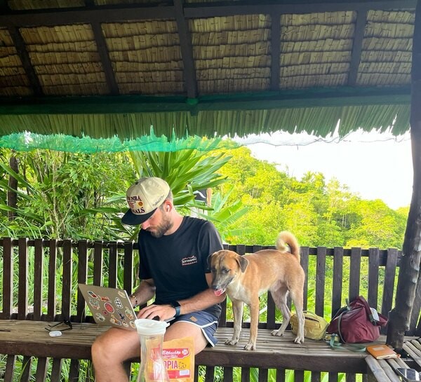 Me looking very focused in front of a laptop. Next to me on the bench stands a dog with his tongue out.