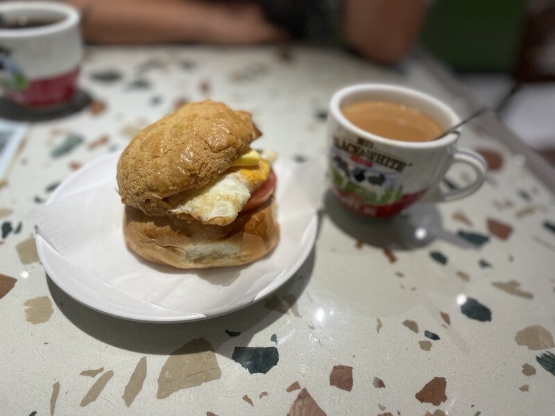 "On a table is a plate with a pineapple bun. Next to it is a cup of milk tea."