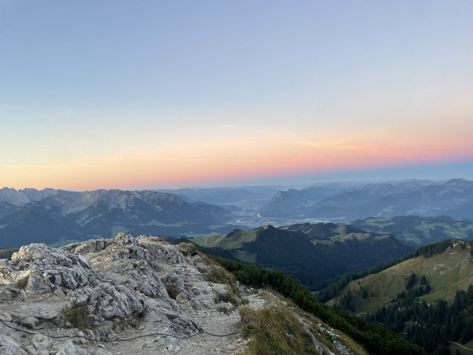 "A mountain landscape at dawn, showing rugged rocks in the foreground and a mountain valley above it."